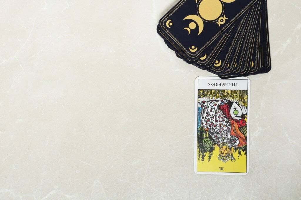 Baralho de tarot com a carta da Imperatriz invertida em primeiro plano sobre uma superfície de mármore, acompanhada por um monte de cartas com a parte de trás à mostra, exibindo luas crescentes e minguantes sobre um fundo preto.