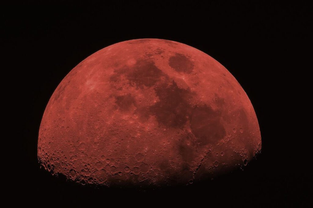 Imagem da Lua tingida de vermelho, sugerindo uma Lua de sangue, com detalhes de crateras visíveis, contra um fundo preto