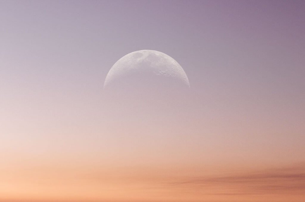 Imagem da Lua em fase crescente contra um céu alaranjado ao amanhecer.