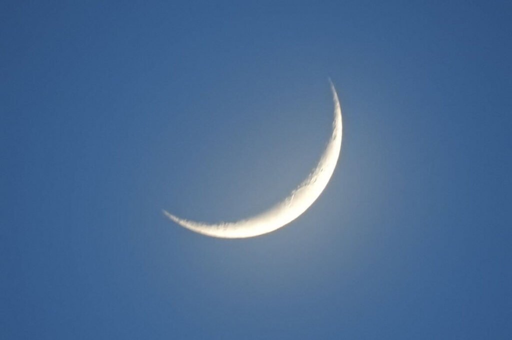 Imagem da Lua em fase crescente contra um céu azul intenso.